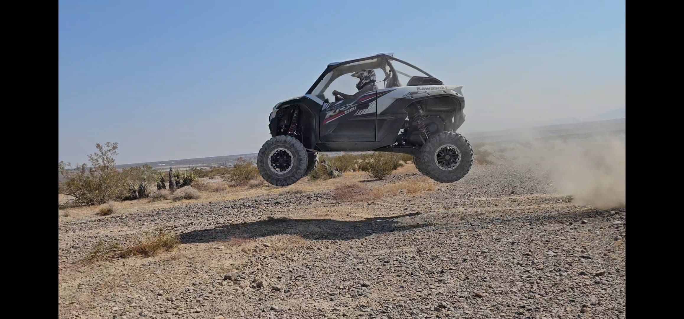 Kawasaki KRX 1000 side-by-side catching big air off a jump on a desert gravel trail